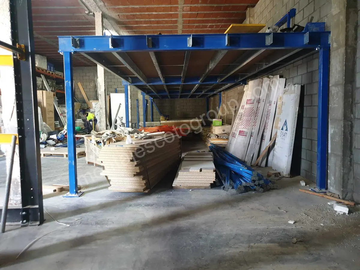 Estructura azul de una entreplanta metálica en una nave, con material apilado debajo